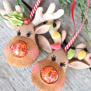 Puede incluir: Dos adornos de reno de fieltro con cinta roja y blanca a rayas. Cada reno tiene un caramelo de chocolate envuelto en papel de aluminio rojo para la nariz.