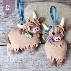 May include: Two brown felt Highland Cow ornaments with a tartan ribbon. One cow has a bell and the other has a purple flower.
