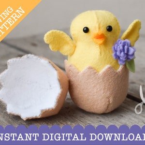 May include: A felt sewing pattern for a chick in an eggshell. The chick is yellow with black eyes and an orange beak. The eggshell is brown with a white interior. The chick has a purple flower on its wing.