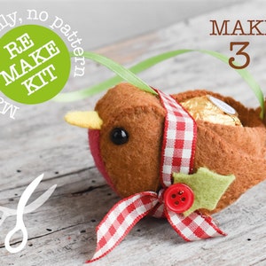 May include: A felt robin ornament with a red and white checkered ribbon, green felt leaves, and a red button. The robin is holding a chocolate treat inside. The ornament is labeled "MAKE 3" and "RE MAKE KIT, materials only, no pattern".