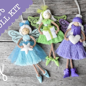 May include: Three handmade yarn angel ornaments with wooden wings and colorful yarn hair. The angels are holding a white star, a white heart, and a white gift box. The ornaments are hanging from a wooden surface.