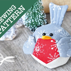 May include: A grey and red fabric bird with a white snowflake pattern. The bird has a yellow beak and black eyes. The bird is a sewing pattern.