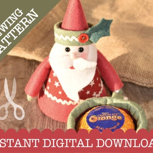 May include: A red and white felt Santa Claus ornament with a green hat and holly. The Santa is holding a chocolate orange in a green felt bag. The text "Made with Real Chocolate Orange" is printed on the orange.