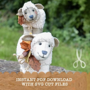 May include: Two white felt sheep with brown eyes and noses. The smaller sheep is sitting on top of the larger sheep. Both sheep have brown felt leaves and acorns attached to them.