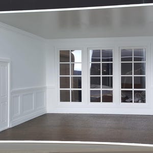 Puede incluir: Una habitación blanca en miniatura con una puerta y tres ventanas grandes. Las ventanas tienen un patrón de cuadrícula. Las paredes son blancas con molduras decorativas. El suelo es de color marrón oscuro.