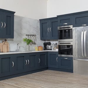 May include: A miniature kitchen with navy blue cabinets, stainless steel appliances, and a white countertop. Includes a fridge, oven, and microwave. The kitchen has a sink, cutting boards, and decorative items.