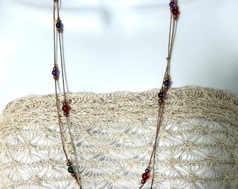 May include: A layered necklace with a delicate gold chain. The necklace features small, colorful beads in red, green, and purple. The necklace is displayed on a white mannequin, showcasing the jewelry's design and color.