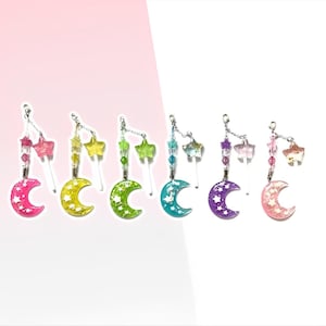 May include: Seven colorful crescent moon charms with star and lollipop accents. Each charm features a white crescent moon with white stars on a colorful background. The charms are attached to silver chains.