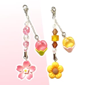 Puede incluir: Dos pulseras con dijes con dijes de flores rosas y amarillas, dijes de corazón rosas y amarillos y cuentas transparentes y de colores.