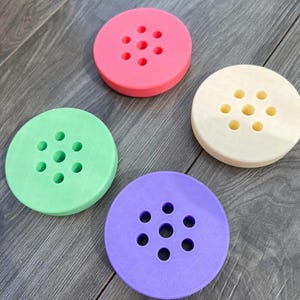 Puede incluir: Cuatro discos redondos de espuma de colores diferentes con varios agujeros en el centro. Los discos son rosa, verde, crema y morado.