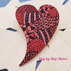 May include: A red heart-shaped wooden ornament with a black and red intricate design. The ornament is decorated with glitter and has a glossy finish.