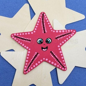 Op de afbeelding: Een roze en zwarte zeester met een glimlachend gezicht en blauwe ogen. De zeester is geschilderd met witte stippen en zwarte lijnen.