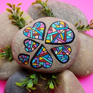 May include: A gray rock painted with five colorful hearts. The hearts are filled with a geometric pattern of pink, blue, yellow, and green.