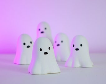 Könnte beinhalten: Fünf weiße Geisterfiguren mit schwarzen Augen und Mündern, in einer Reihe auf einem rosa Hintergrund angeordnet.