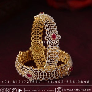 Può includere: Due braccialetti d'oro con intricati disegni di diamanti e rubini. I braccialetti sono impilati l'uno sull'altro e presentano un delicato motivo a filigrana.