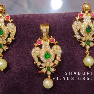 May include: A gold pendant and earrings set with white stones, green and red accents, and a pearl drop. The pendant and earrings feature a floral design.