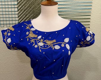 Op de afbeelding: Een koninklijk blauwe blouse met korte mouwen en een ronde hals. De blouse is versierd met witte parels en gouden borduurwerk van vogels en takken.