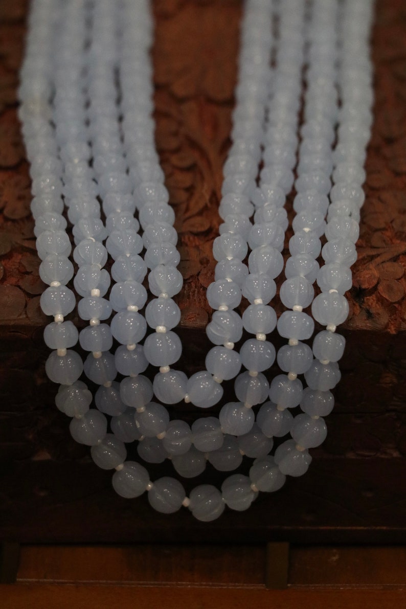 May include: A multi-strand necklace made of light blue beads. The beads are round and have a slightly textured surface.