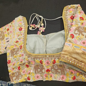 Puede incluir: Una blusa gris bordada con un diseño floral y de elefantes. La blusa tiene cuello redondo y mangas cortas. El bordado está hecho en tonos de rosa, amarillo y rojo.