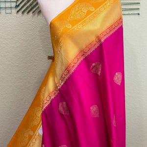 Könnte beinhalten: Ein gelber und rosa Seiden-Sari mit goldener Stickerei. Der Sari hat ein traditionelles Design mit Paisley-Motiven.