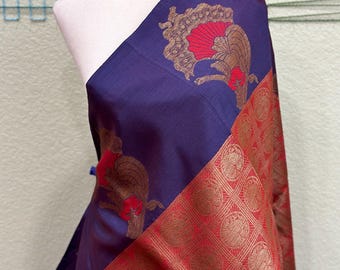 Puede incluir: Una tela de seda morada y roja con un diseño tejido dorado. La tela presenta un patrón repetitivo de pavos reales estilizados con abanicos rojos y detalles dorados. La tela está drapeada sobre un maniquí blanco.