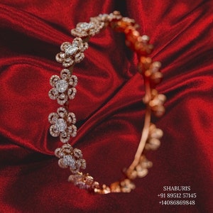 May include: A gold bangle bracelet featuring a delicate floral design set with sparkling diamonds. The bracelet is displayed against a red satin backdrop.