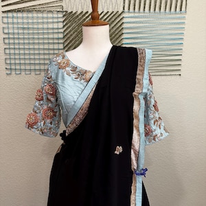 Könnte beinhalten: Ein schwarzer und hellblauer Sari mit goldenen Verzierungen und Blumenstickereien. Der Sari ist über eine Schaufensterpuppe drapiert.