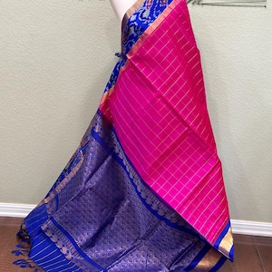 Könnte beinhalten: Ein rosa-blaues Seiden-Sari mit einem karierten Muster und einem goldenen Rand. Das Sari hat ein blaues und weißes Ikat-Muster auf dem Pallu.