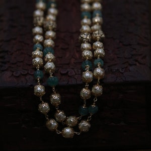 May include: A double strand necklace with gold beads and white pearls. The beads are decorated with intricate designs.