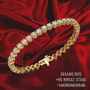 May include: A gold tennis bracelet with round diamonds set in a continuous line. The bracelet has a clasp closure. The bracelet is on a red velvet background.