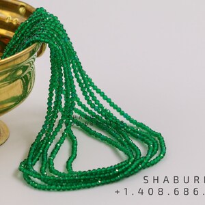 May include: A strand of green gemstone beads in a bowl. The beads are faceted and have a shiny finish. The bowl is made of brass and has a gold finish. The text "SHABURIS +1.408.686.9848" is visible in the image.