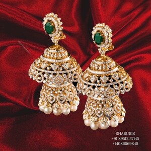 May include: A pair of gold earrings with a multi-tiered design, featuring a green gemstone at the top and white pearls at the bottom. The earrings are adorned with intricate details and sparkling diamonds.