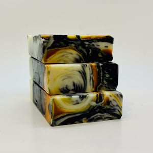 May include: Four bars of handmade soap stacked on top of each other. The soap is a swirl of black, white, and gold.