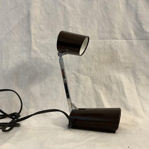 May include: A black desk lamp with a flexible arm and a black shade. The lamp has a silver base and a black cord.