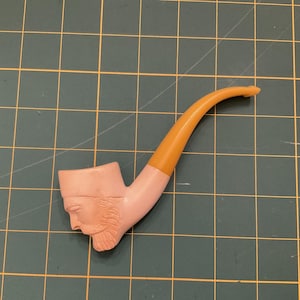 Peut inclure: Une pipe sculptée rose et orange avec un visage humain sur le bol.