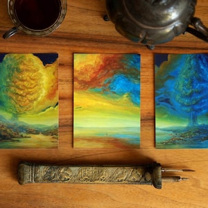 Pode incluir: Três pinturas de paisagens com cores vibrantes de amarelo, laranja e azul. Um porta-canetas decorativo com entalhes e uma xícara de chá também são visíveis em uma superfície de madeira.