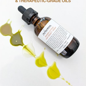 May include: A brown glass bottle of "Anagen Extend Hair Density Serum" with a black dropper, and a white label. The bottle is surrounded by yellow and green oil droplets. The text "100% ORGANIC, COLD-PRESSED, & THERAPEUTIC-GRADE OILS" is at the top.