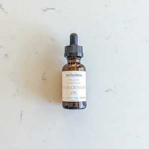 May include: A brown glass bottle with a dropper top containing organic unrefined sea buckthorn oil. The bottle is labeled "The Potter's Mixtress" and lists the oil as unrefined, vegan, and chemical-free. The bottle contains 30 ml or 1 oz of oil.