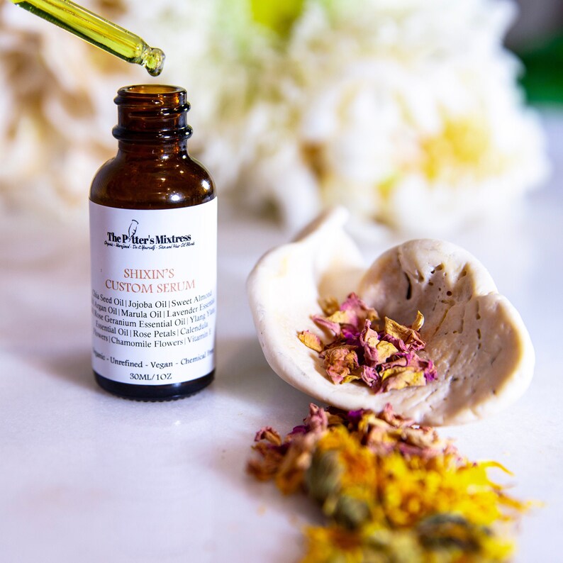 Puede incluir: Una botella de vidrio marr&oacute;n con un gotero, etiquetada como "The Piter's Mixtress Shixin's Custom Serum". La botella est&aacute; sobre una superficie blanca con p&eacute;talos de rosa secos y flores amarillas.