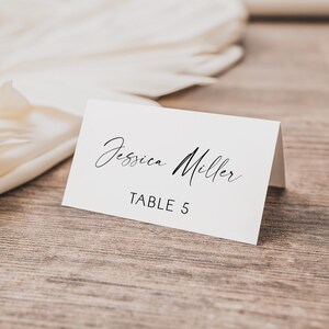 Puede incluir: Tarjeta blanca con caligrafía negra que dice "Jessica Miller" y "Mesa 5".