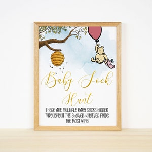 May include: A Winnie the Pooh themed baby shower game sign with a watercolor background. The sign says "Baby Sock Hunt" and includes a cartoon image of Winnie the Pooh holding a pink balloon and Piglet.
