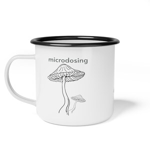 May include: White enamel mug with a black rim. The mug has a black line drawing of a mushroom with the word "microdosing" above it.