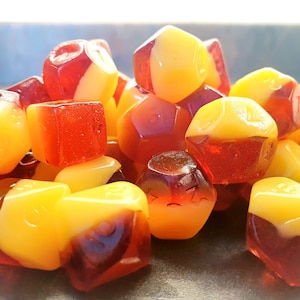 May include: A pile of red and yellow candy shaped like dice. The candy is translucent and has a glossy finish.