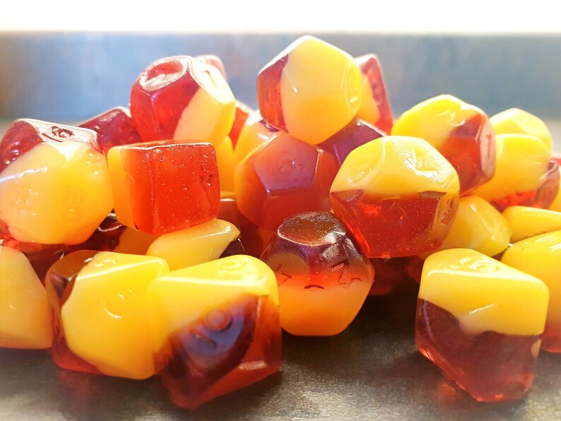 May include: A pile of red and yellow candy shaped like dice. The candy is translucent and has a glossy finish.