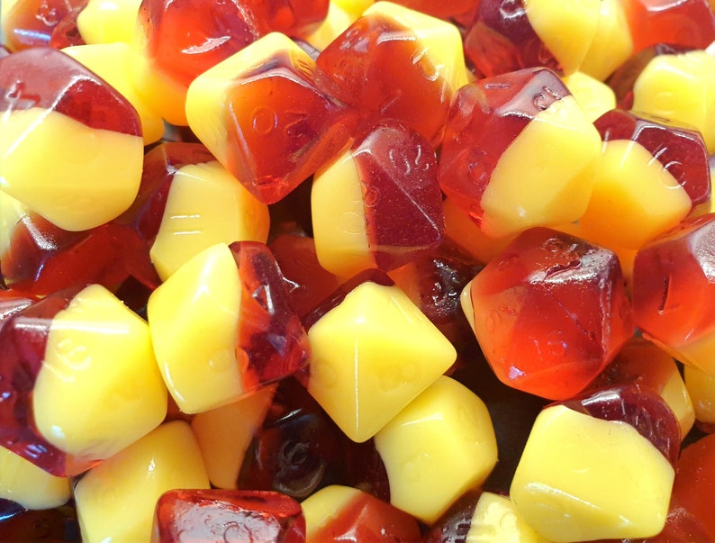 May include: A close-up of a pile of red and yellow candy shaped like dice. The candy is translucent and has a glossy finish.