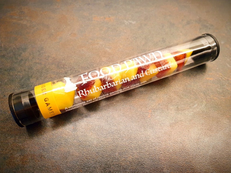 May include: A clear plastic tube filled with yellow and red candy shaped like dice. The tube has a white label that reads "FOOD PAWD Rhubarbarian and Custard A complete set of replica gaming dice made with rhubarb and custard."
