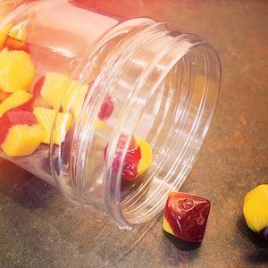 May include: A clear plastic jar with a red and yellow dice set spilling out. The dice are multi-sided and have a red and yellow color scheme.