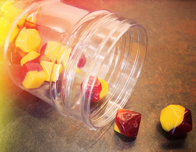 May include: A clear plastic jar with a red and yellow dice set spilling out. The dice are multi-sided and have a red and yellow color scheme.