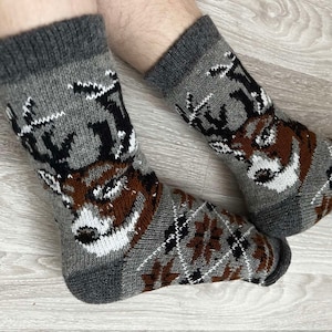May include: A pair of gray wool socks with a brown deer pattern. The socks have a black and white geometric pattern around the ankle.