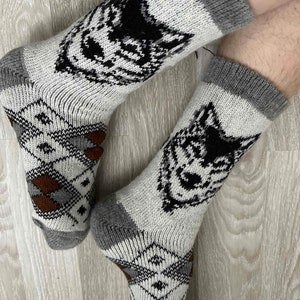 May include: A pair of grey and white wool socks with a black wolf design. The socks have a brown and grey geometric pattern on the bottom.